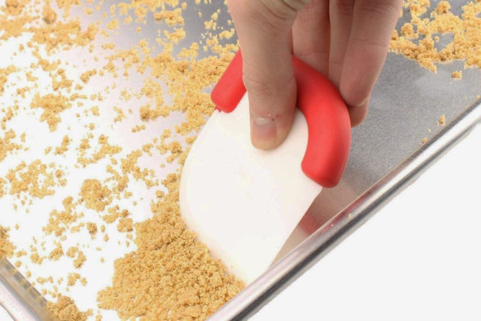 Person using the scraper to scrape a baking pan.